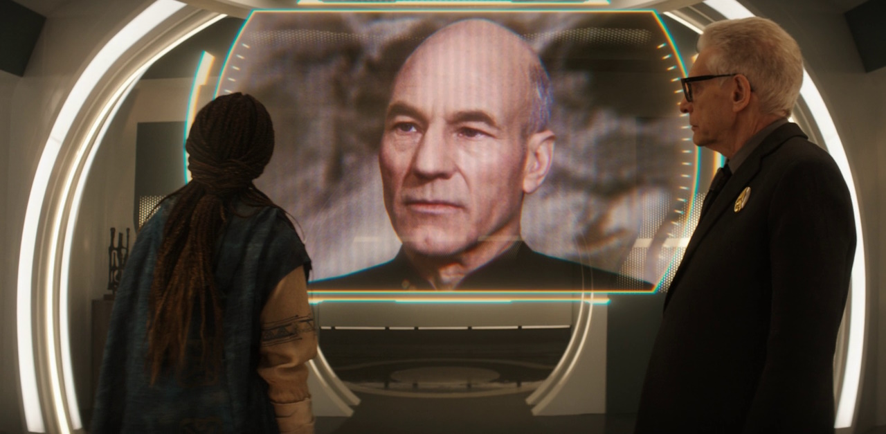 Still frame from Star Trek: Discovery Season 5 (2024) showing Burnham and Kovich looking at a holographic image of Captain Picard.