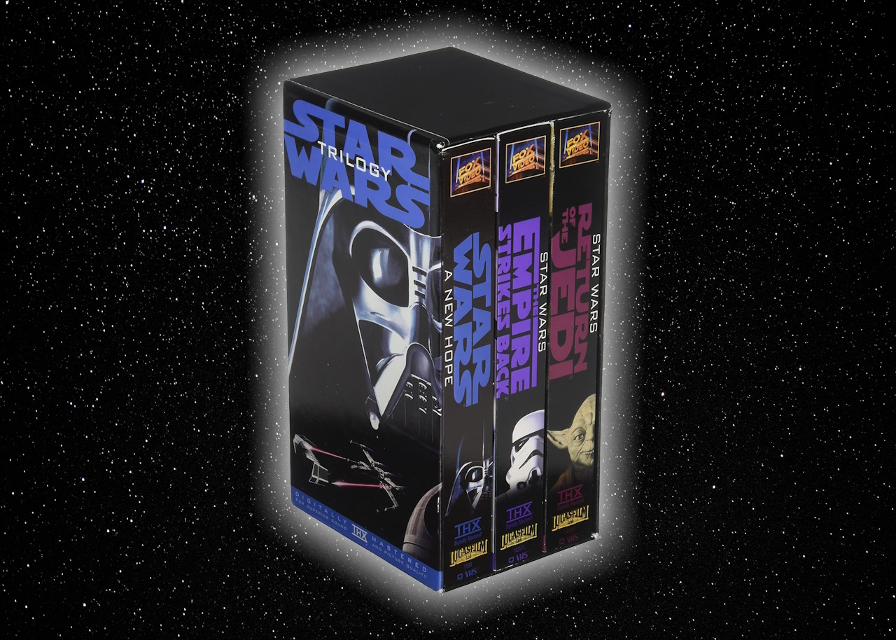The Star Wars trilogy on VHS on a starry background.
