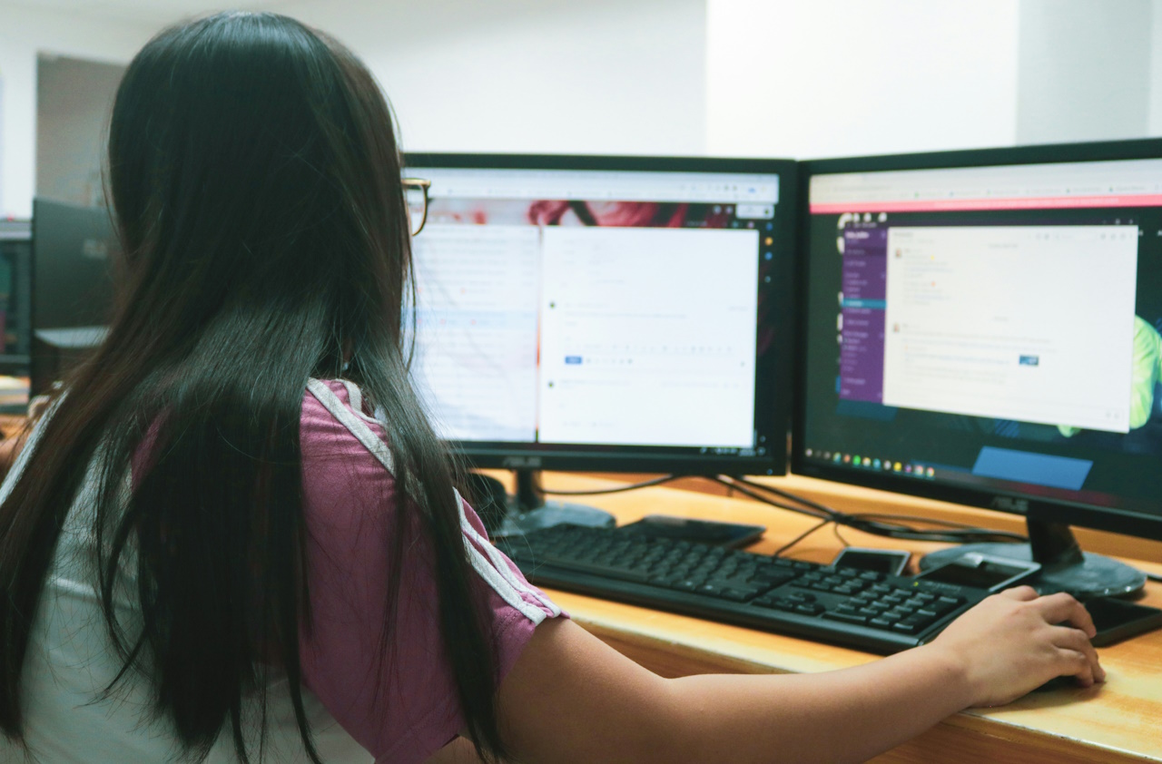 Promo photo of a woman working on a computer with two monitors.