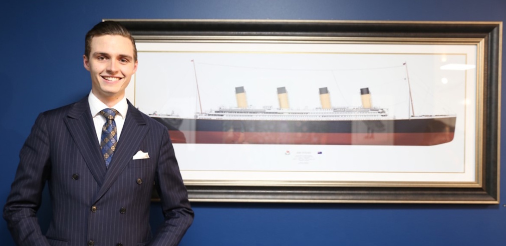 Promo photo for Oceanliner Designs showing a man in a suit next to a painting of the RMS Titanic.