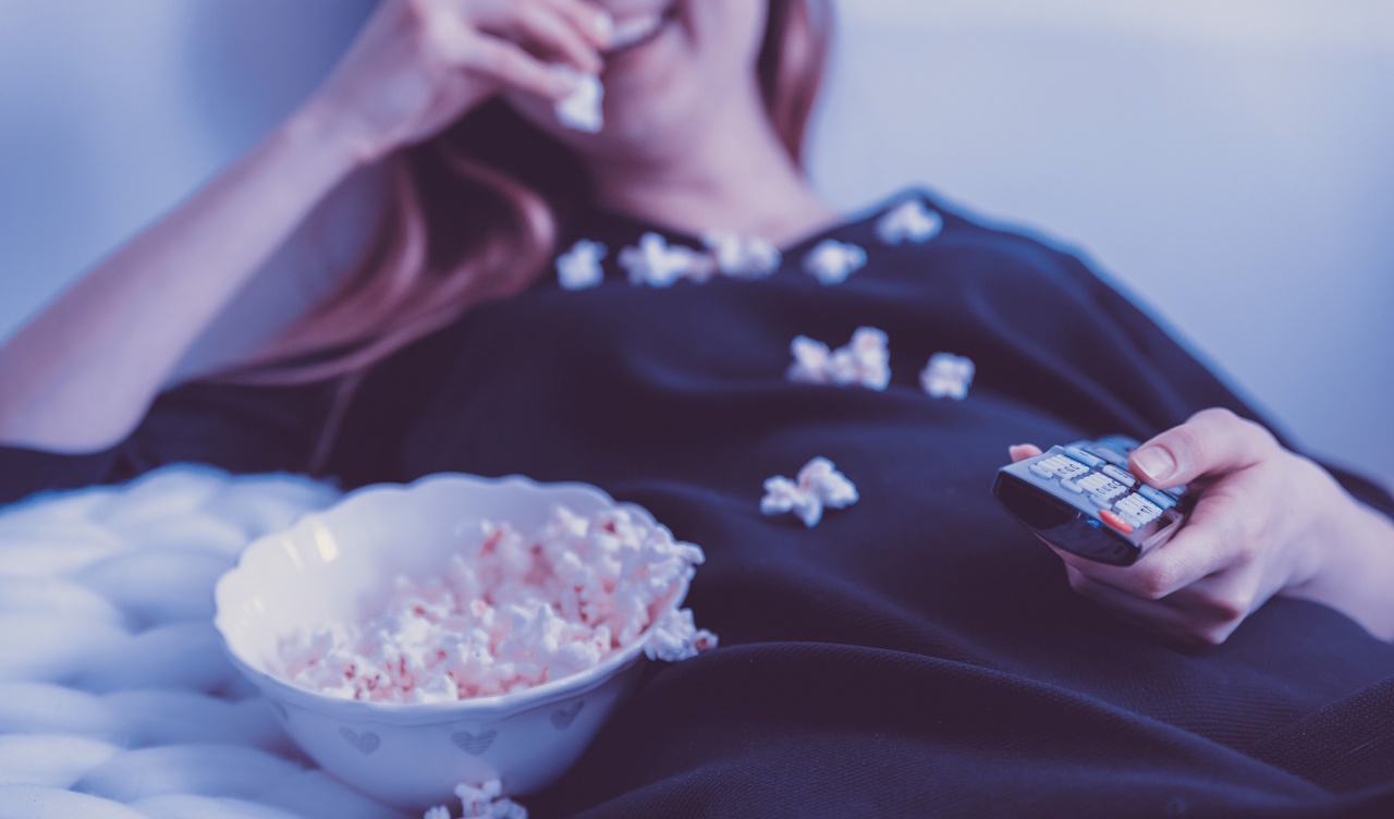 Stock photo of a woman holding a television remote while eating popcorn.