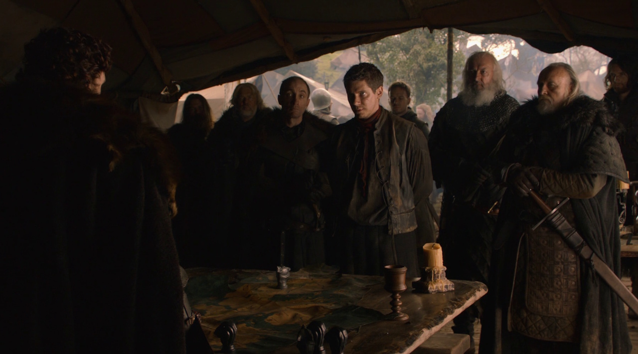 Still frame from Game of Thrones Season 2 showing several characters addressing Robb Stark.