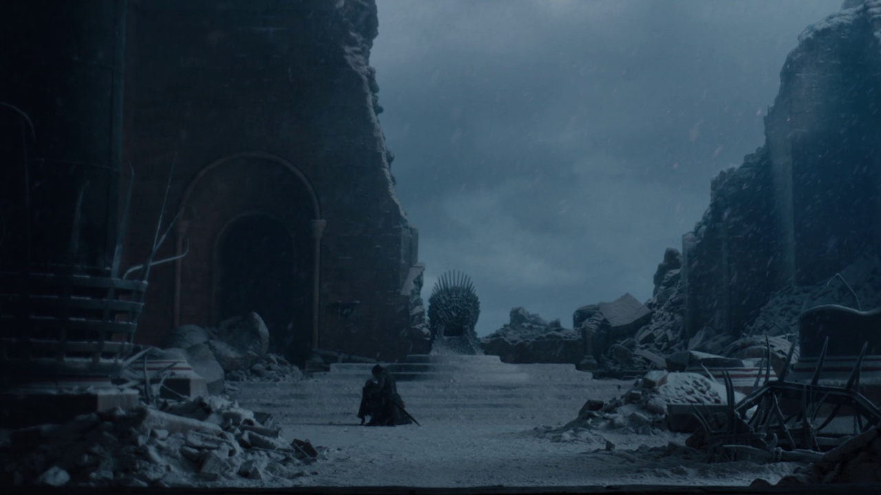 Still frame from the Game of Thrones series finale showing the damaged throne room, the Iron Throne, Jon Snow, and Daenerys Targaryen.