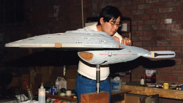 Behind-the-scenes photo showing Michael Okuda working on a model of the USS Voyager.