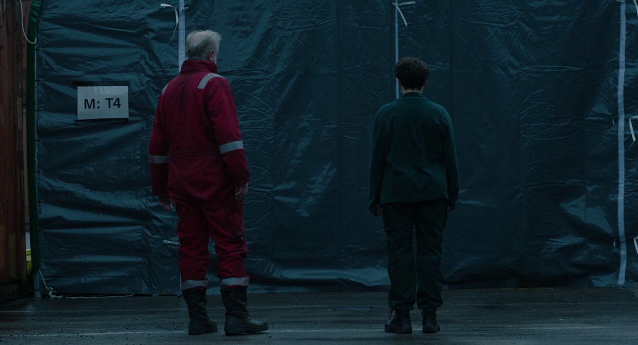 Still frame from The Rig Season 2 (2025) showing Hutton and Cat standing in front of the mortuary tent.