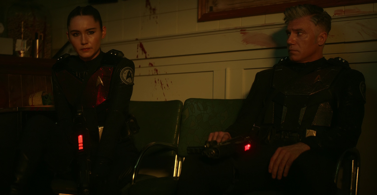 Still frame from Star Trek: Strange New Worlds Season 2 Episode 10 (2023) showing La'an and Captain Pike sitting on a bench, taking shelter.