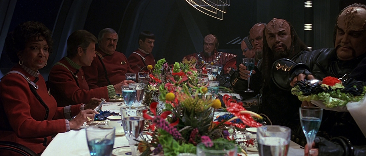 Still frame from Star Trek VI: The Undiscovered Country showing Starfleet officers and Klingons at a diplomatic dinner.