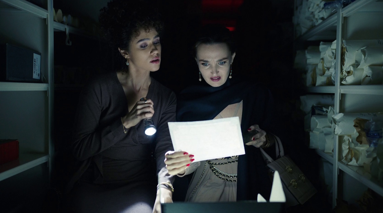 Still frame from Megalopolis (2024) showing two characters looking at a document with a flashlight.