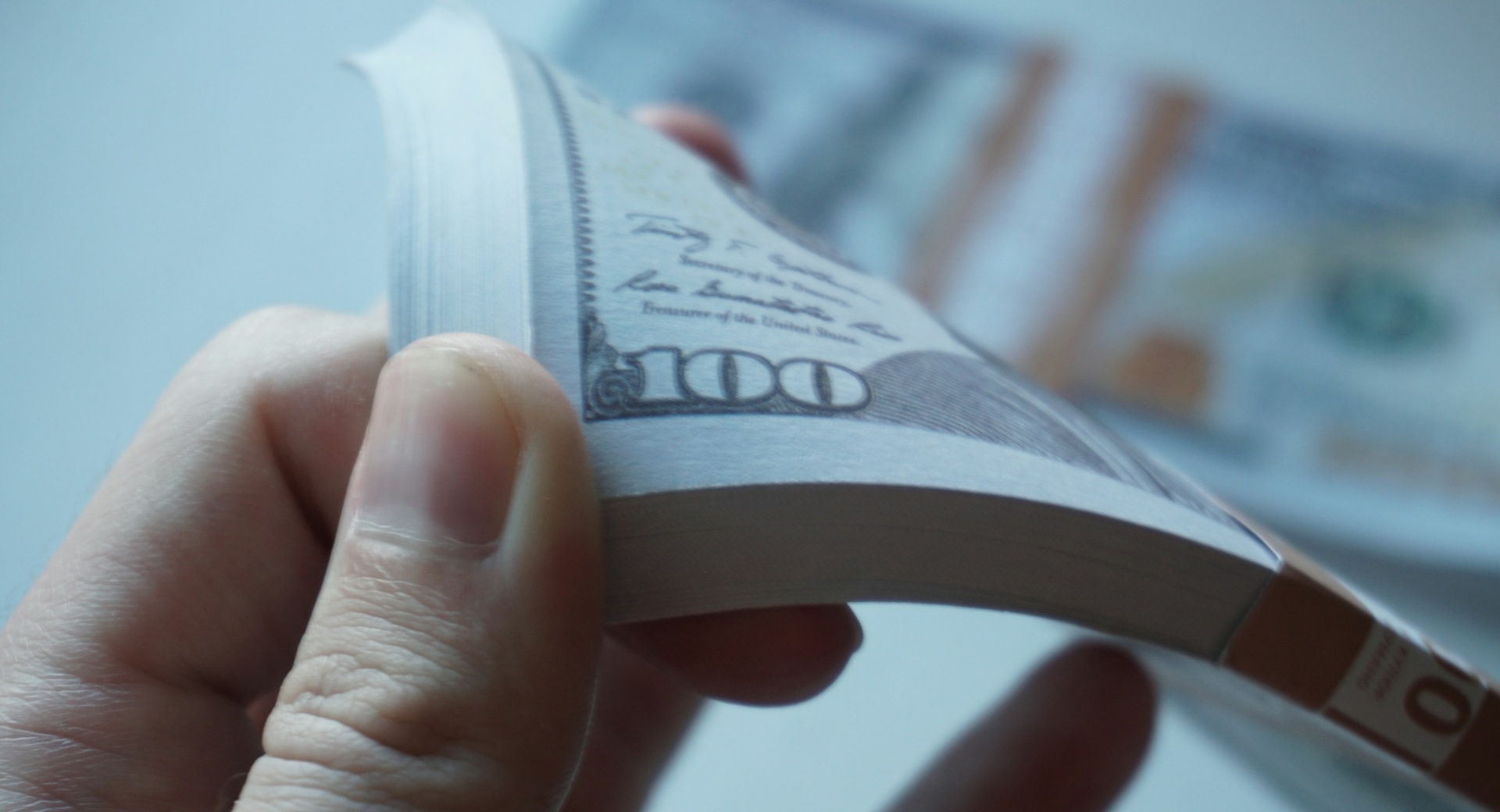 Stock photo of a hand holding a stack of $100 bills.