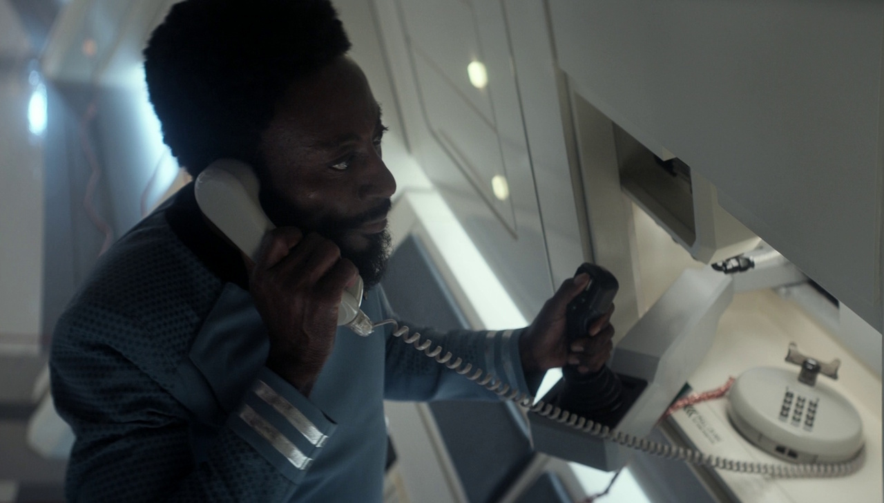 Still frame from Star Trek: Strange New Worlds 3x06: The Sehlat Who Ate Its Tail showing Dr M'Benga on the phone.