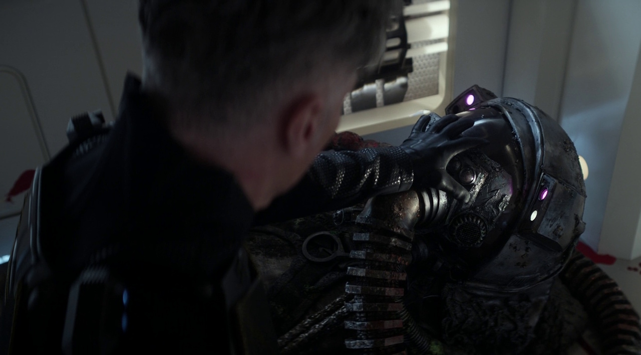 Still frame from Star Trek: Strange New Worlds 3x06: The Sehlat Who Ate Its Tail showing Pike reaching for the helmet of a dead scavenger.