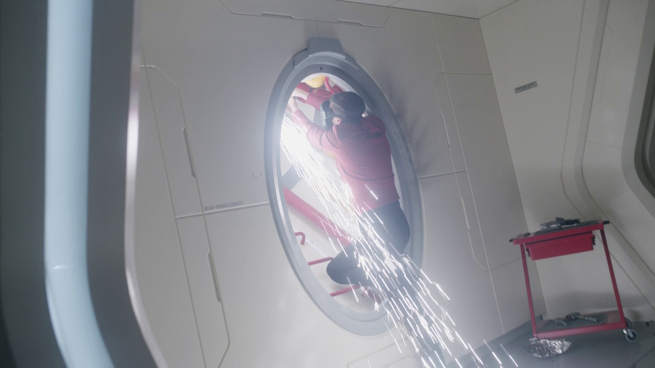 Still frame from Star Trek: Strange New Worlds S03E07 "What Is Starfleet?" showing an engineer reparing damage to the Enterprise.