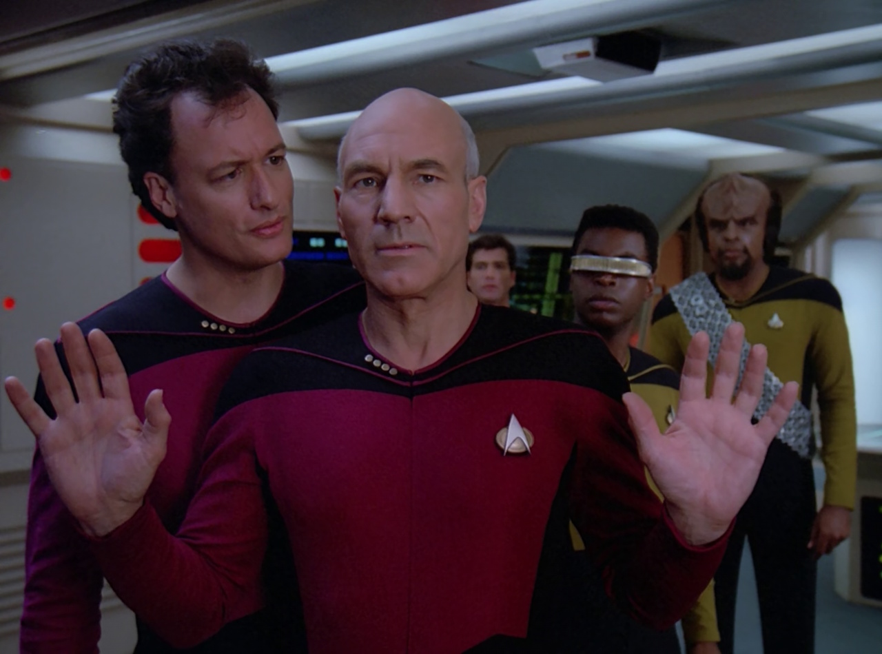 Still frame from Star Trek: TNG showing Picard, Q, Geordi, and Worf in engineering.