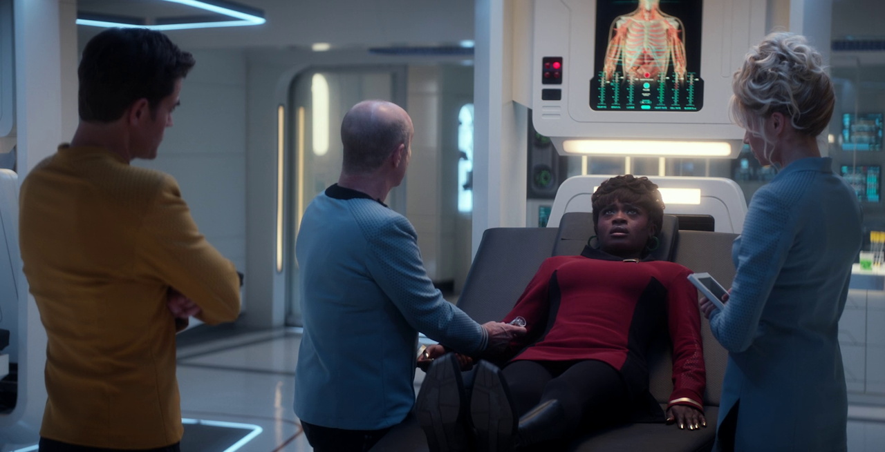Still frame from Star Trek SNW 4x10 showing Kirk, Uhura, Dr Boyce, and Chapel at a bio-bed in sickbay